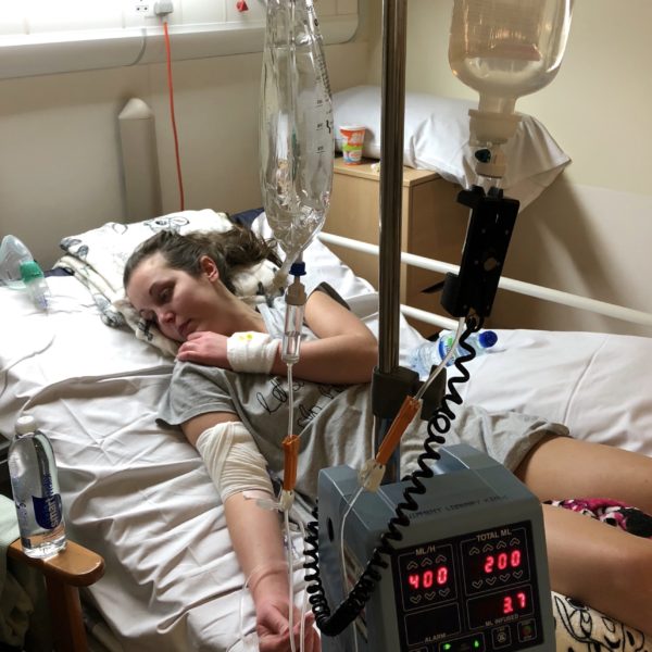 Lauren lying on a hospital bed receiving various intravenous treatments. 