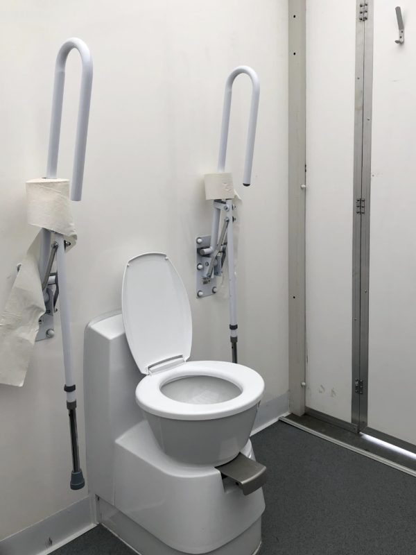Folding grab rails surrounding a white toilet with room for wheelchair transfers. 