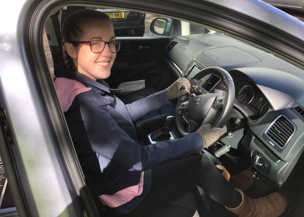 Lauren is sat in the driver's seat of a grey SEAT Alhambra, whilst holding a steering ball and hand accelerator.